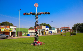 O monumento temporário no canteiro da Via Norte com a Av. Castelo Branco é uma cruz formada por capacetes e objetos que remetem a acidentes de trânsito, destacando o impacto dessas tragédias.