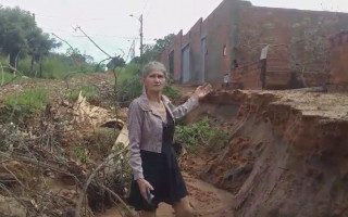 Dona Maria das Dores Lima mostra cratera que ameaça derrubar poste de energia e o muro de sua casa. 