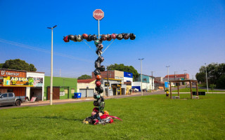 O monumento temporário no canteiro da Via Norte com a Av. Castelo Branco é uma cruz formada por capacetes e objetos que remetem a acidentes de trânsito, destacando o impacto dessas tragédias.