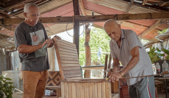 Antônio Luiz Ribeiro da Neves, conhecido como Tauru, ao lado do pai, José Fernandes Neves, o Seu Zeca, mestre artesão de Porto Nacional. A produção de móveis em madeira de buriti segue como ofício familiar, mantendo a prática ativa entre gerações 